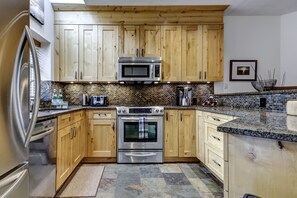 A modern kitchen with wooden cabinets, a stainless steel oven, and a microwave. - Snowy Creek 30 - Ski in Ski out, Private Hot Tub, Short Walk to Whistler Village (Whistler)