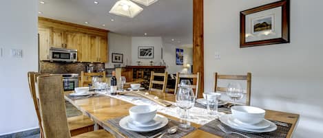 Un comedor con una larga mesa de madera dispuesta para una comida, rodeado de sillas de madera.