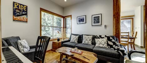 A living room with a piano, a sofa, a coffee table, and a large window.