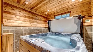 L’intérieur d’un chalet en bois, avec un jacuzzi, des murs recouverts de pierres et une fenêtre équipée de stores.