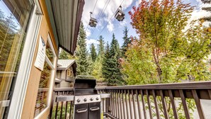 Un balcon doté d’un barbecue, d’une balustrade en bois et offrant une vue sur les arbres, avec une télécabine visible au loin.