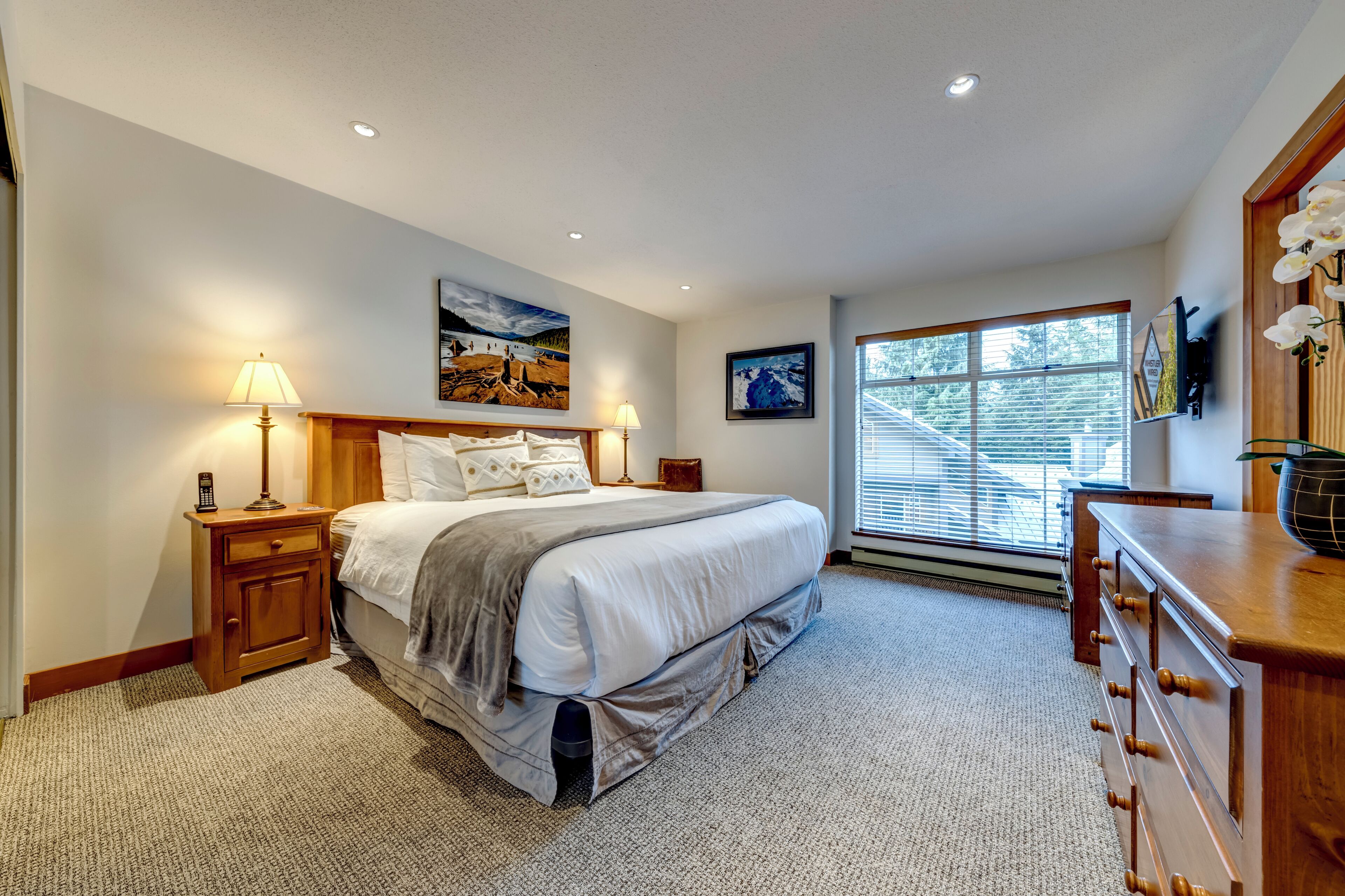 Une chambre à coucher avec un grand lit, des tables de chevet, une commode et une fenêtre avec des stores.
