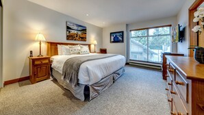 Une chambre à coucher avec un grand lit, des tables de chevet, une commode et une fenêtre avec des stores.