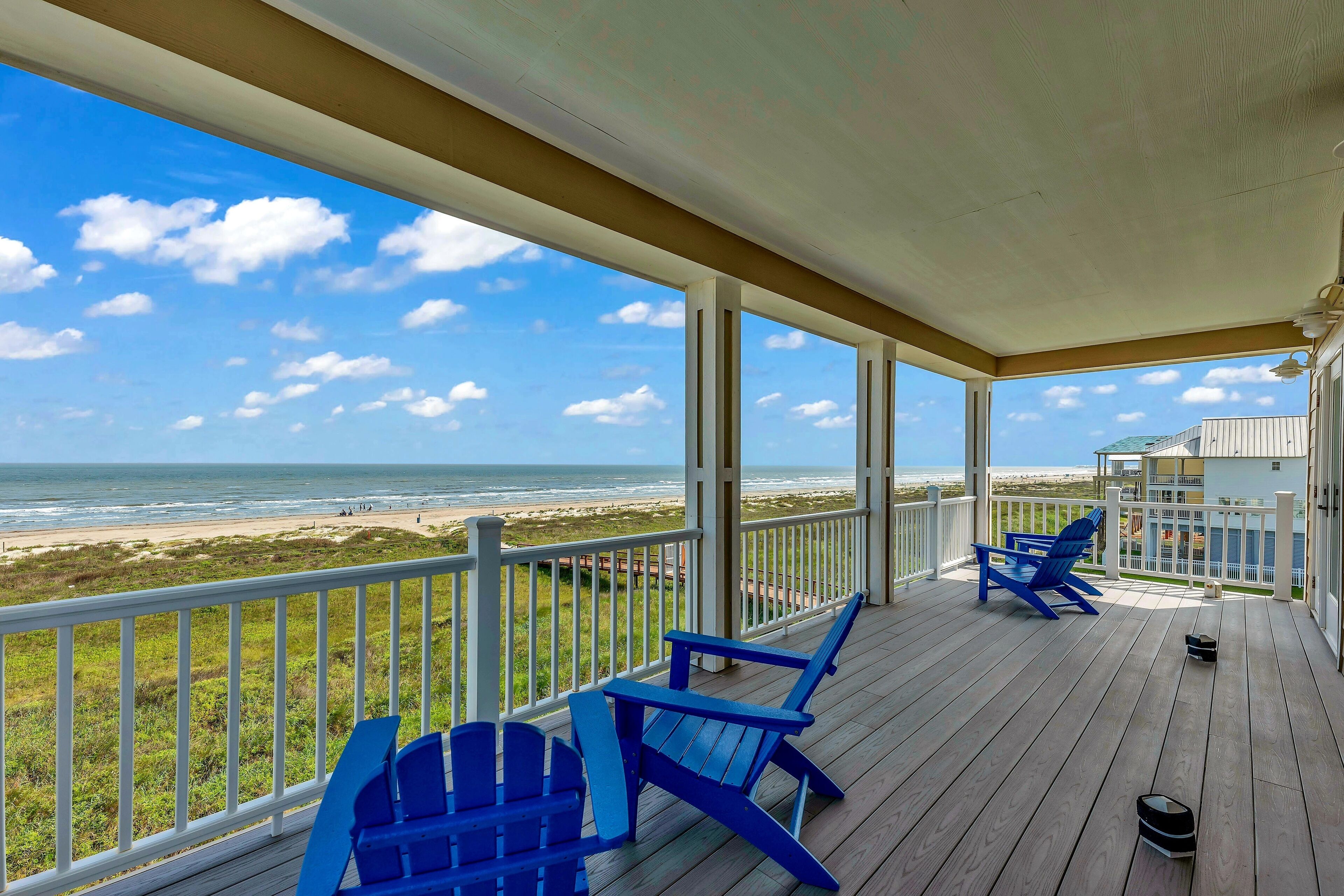 A wooden deck with blue Adirondack chairs overlooking a beach.