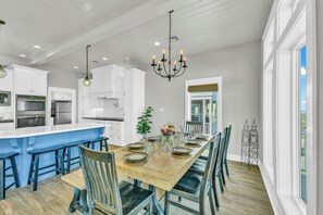 A spacious kitchen with white cabinets, a central island, and a dining area with a wooden table set for six. - Top-Rated Beachfront • Steps to Sand • Hot Tub • Elevator • Firepit • Sleeps 16 (Galveston)