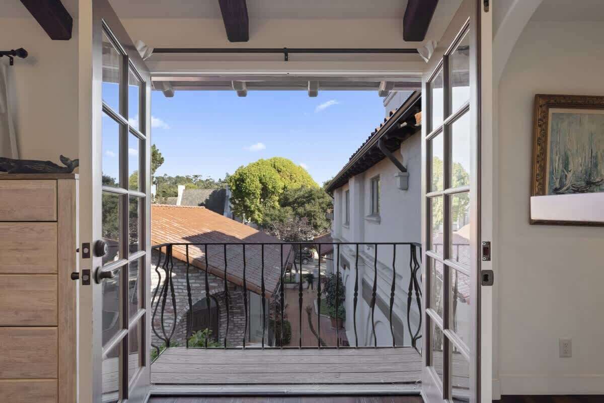 Une porte ouverte donnant sur une cour, une terrasse en bois et un bâtiment avec un toit en tuiles.