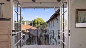 Une porte ouverte donnant sur une cour, une terrasse en bois et un bâtiment avec un toit en tuiles.