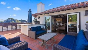 Une terrasse extérieure aménagée avec des meubles en osier, un barbecue et une porte-fenêtre coulissante donnant sur un espace de vie intérieur.
