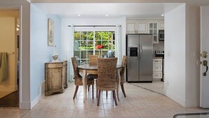 Un coin repas avec une table et des chaises, un réfrigérateur et une vue sur l’extérieur grâce à une porte vitrée.