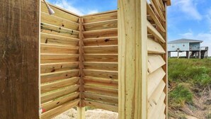 Ein Holzhaus mit geneigtem Dach, wahrscheinlich ein Strandhaus oder eine Berghütte, mit freiem Blick auf ein Haus im Hintergrund.
