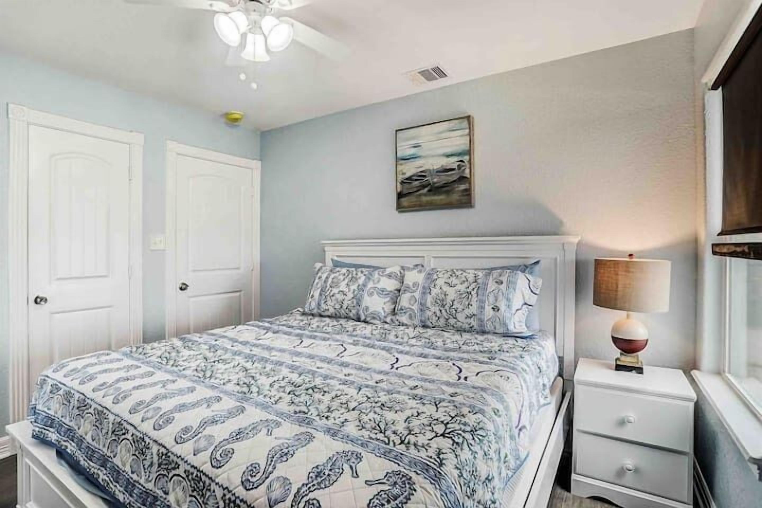 A bedroom with a bed, white nightstands, a lamp, and a painting on the wall.