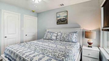 A bedroom with a bed, white nightstands, a lamp, and a painting on the wall.