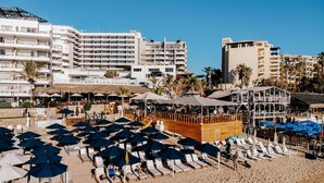 Un hôtel situé en bord de mer, doté de nombreux balcons, de chaises longues, de parasols et d’une terrasse en bois.