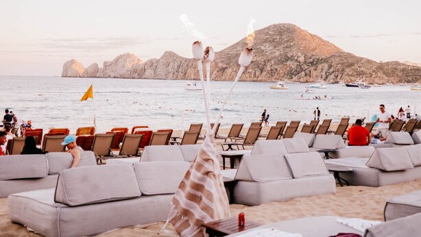 Un espace de détente aménagé au bord de la plage, avec des rangées de sièges confortables et des tables, offrant une vue sur la mer et les collines rocheuses.