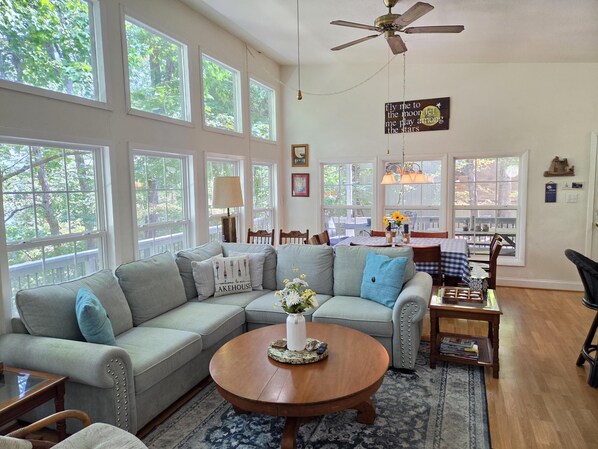 A spacious living room with a large gray sectional sofa, a round wooden coffee table, and a dining area with a checkered tablecloth.