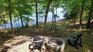 A campsite with a fire pit, two Adirondack chairs, and a bench near a lake surrounded by trees. - Moon Beam-Lakefront-Community Pool & Lost Bridge Marina Nearby (Garfield)