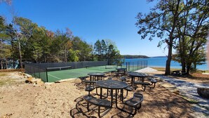 A tennis court with a net, surrounded by picnic tables and benches, with trees and a lake in the background. - Moon Beam-Lakefront-Community Pool & Lost Bridge Marina Nearby (Garfield)