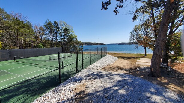 A tennis court with a net, surrounded by gravel and trees, overlooking a body of water. - Moon Beam-Lakefront-Community Pool & Lost Bridge Marina Nearby (Garfield)