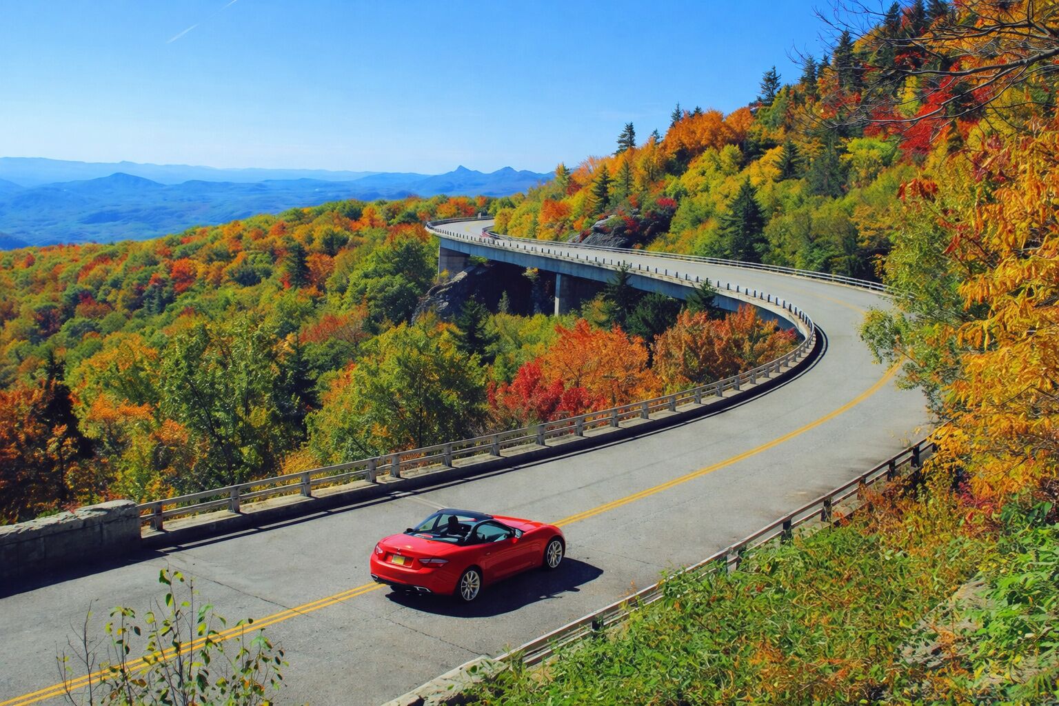 A winding road with a red car, surrounded by autumn foliage and a bridge.