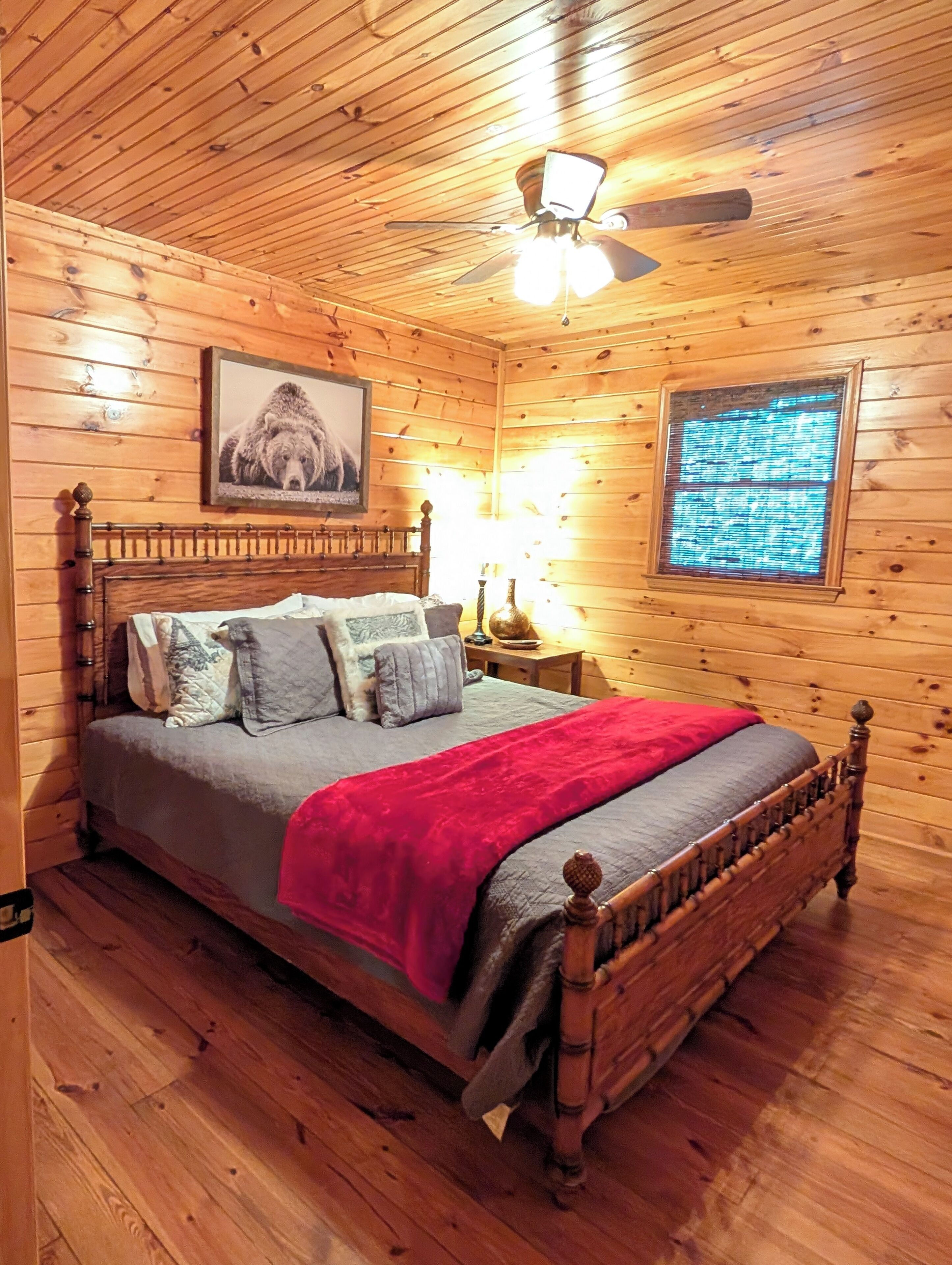 Ein Schlafzimmer einer Holzhütte mit Bett, Nachttisch, Lampe, Deckenventilator und einem gerahmten Bild an der Wand.