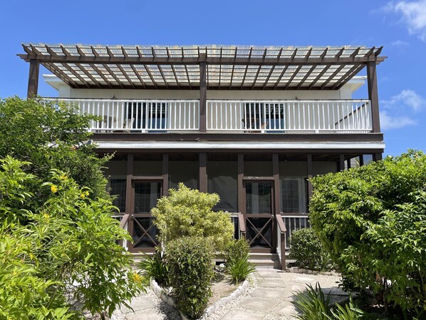 A two-story building with a balcony, a covered porch, and a garden area with various plants.