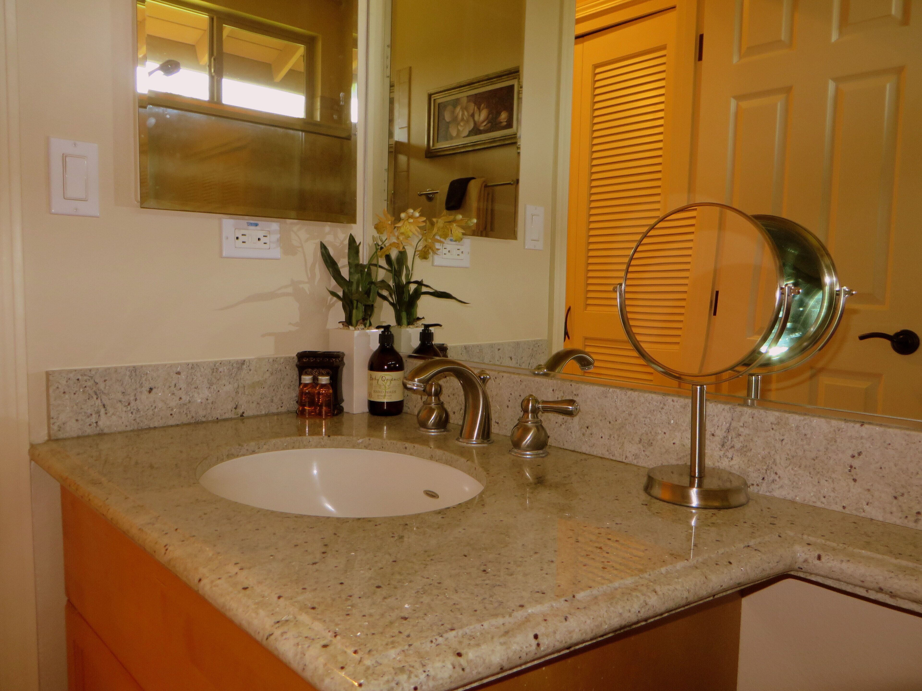 A bathroom with a granite countertop, a white sink, a mirror, and a door with a window above it.
