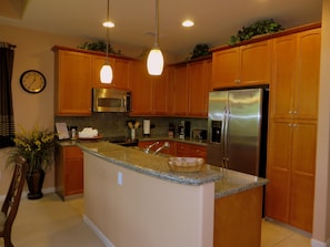 A kitchen with wooden cabinets, stainless steel appliances, granite countertops, and pendant lighting.