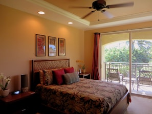 A bedroom with a large bed, a ceiling fan, and a balcony with outdoor furniture.