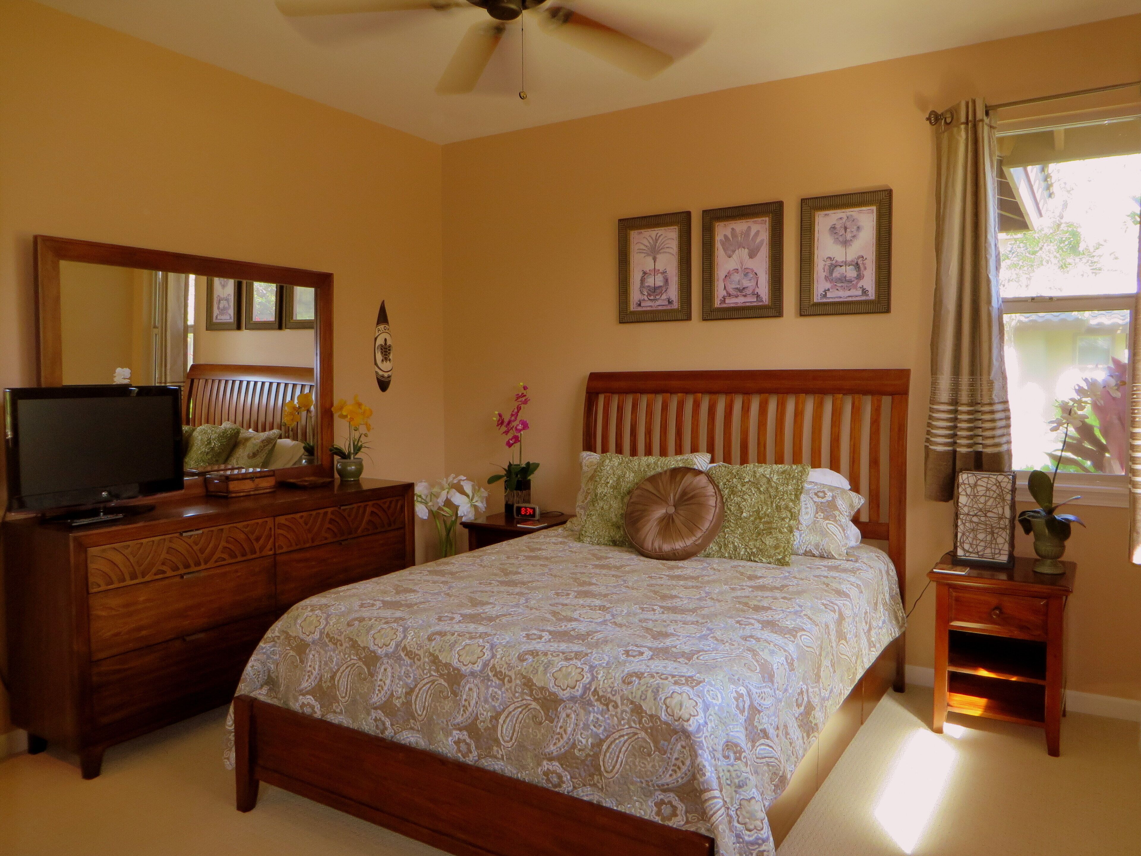 A bedroom with a bed, dresser, TV, and artwork on the walls.