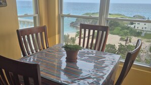 A dining area with a table and chairs, a potted plant, and a view of the ocean through large windows. - Panoramic Private Beachfront Home with Breathtaking Views (Southampton)