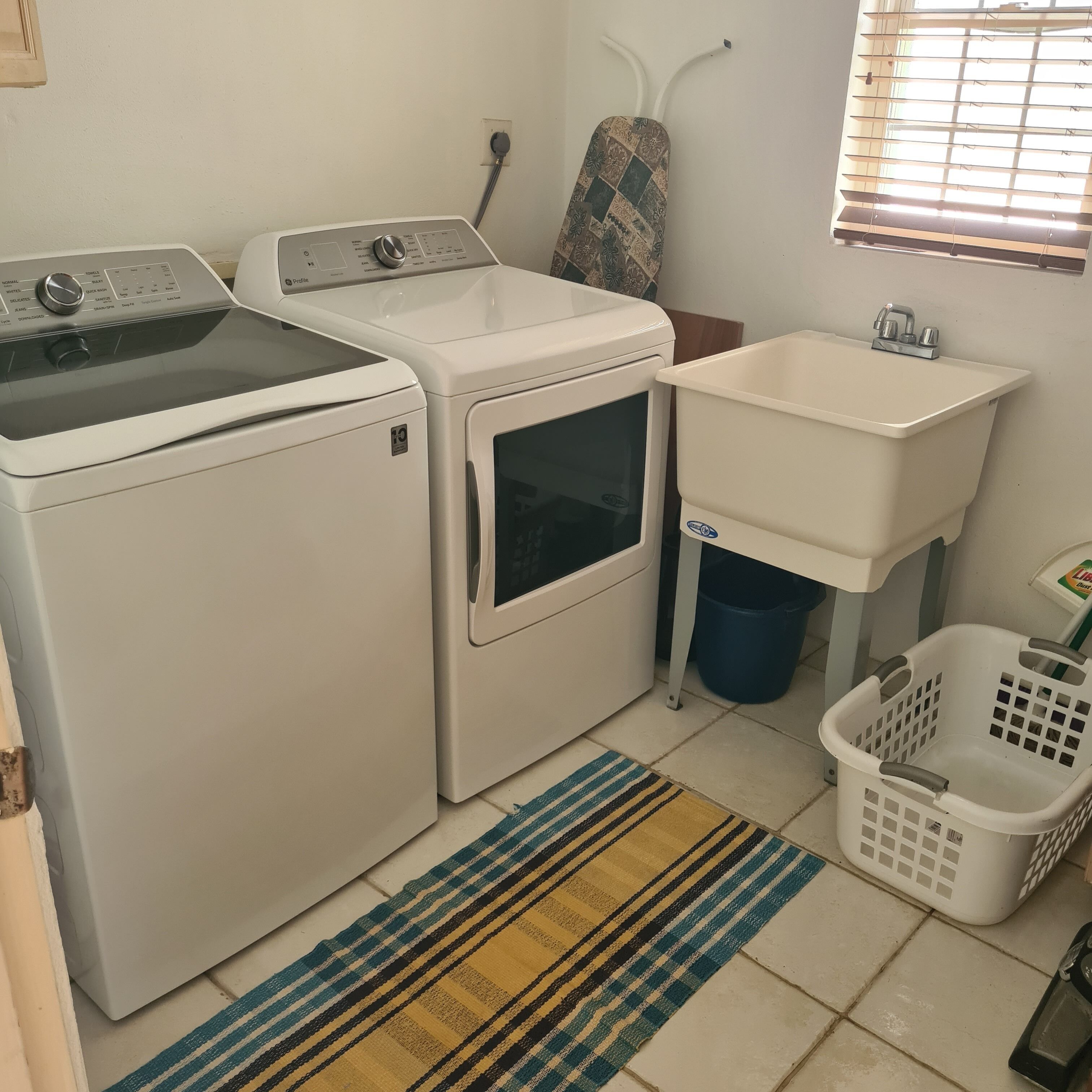 A laundry room with a front-loading washer, a dryer, a sink, and a laundry basket.