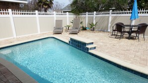 Une piscine rectangulaire dont le bord est recouvert de carreaux, entourée d’une terrasse en briques.