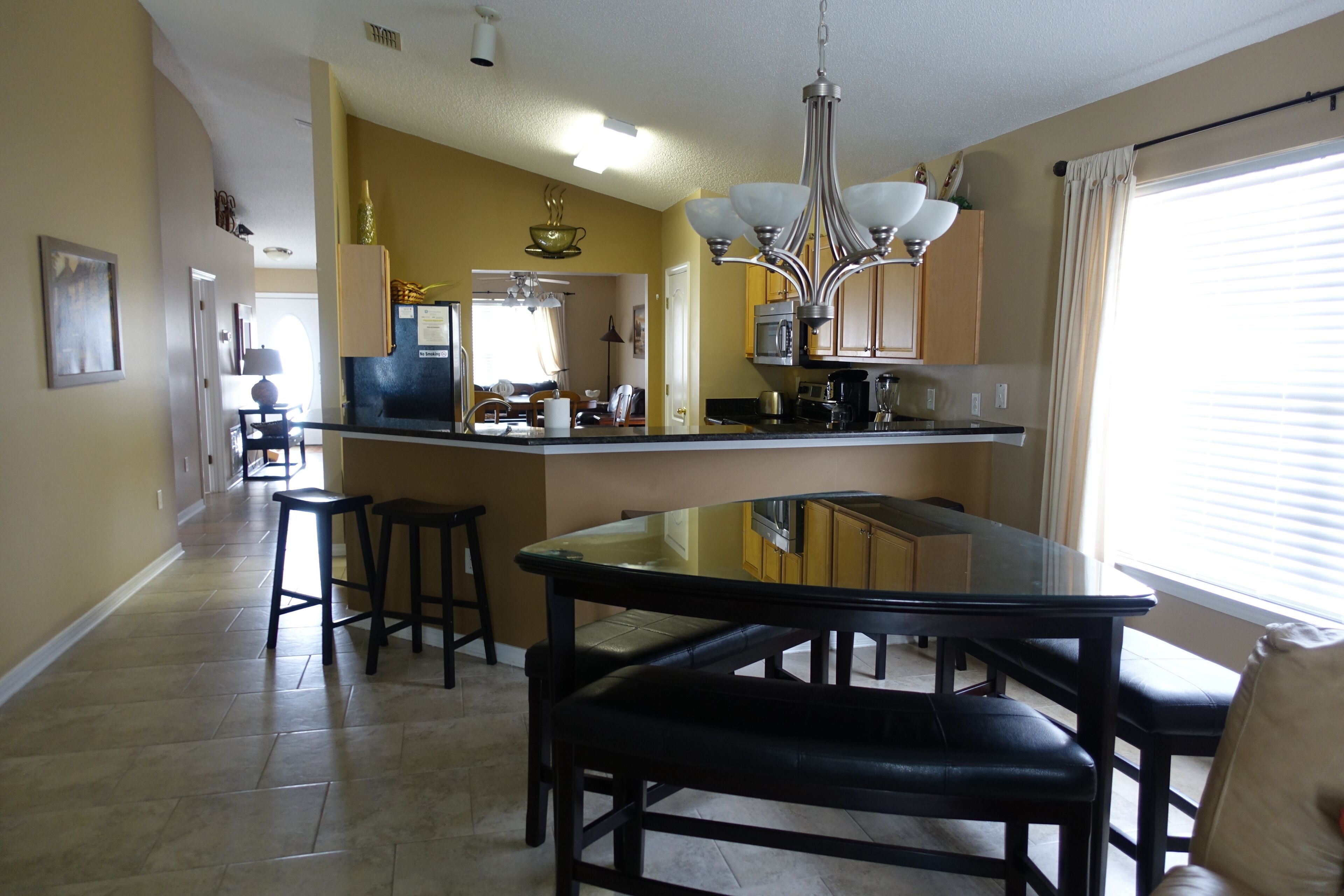 A modern kitchen with a central island, bar stools, and a chandelier.