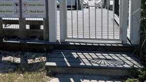 Une entrée fermée par un portail sur lequel est affiché un panneau indiquant « DÉFENSE D’ENTRER », une passerelle en bois et des panneaux indiquant l’emplacement de résidences privées sur la plage.