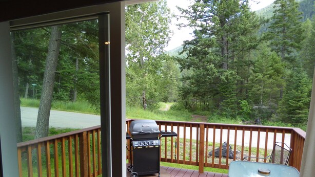 Eine Terrasse mit Grill, Tisch und Stühlen, mit Blick auf ein bewaldetes Gebiet.
