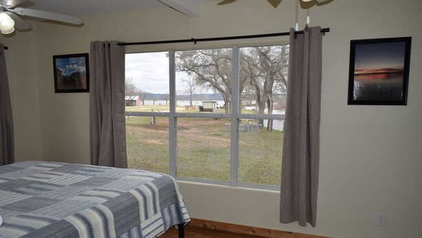 A bedroom with a large window, a bed, a ceiling fan, and a view of a park.