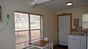 A small kitchen with a dining table and chairs, a window with blinds, and a door with a 'No Smoking' sign.