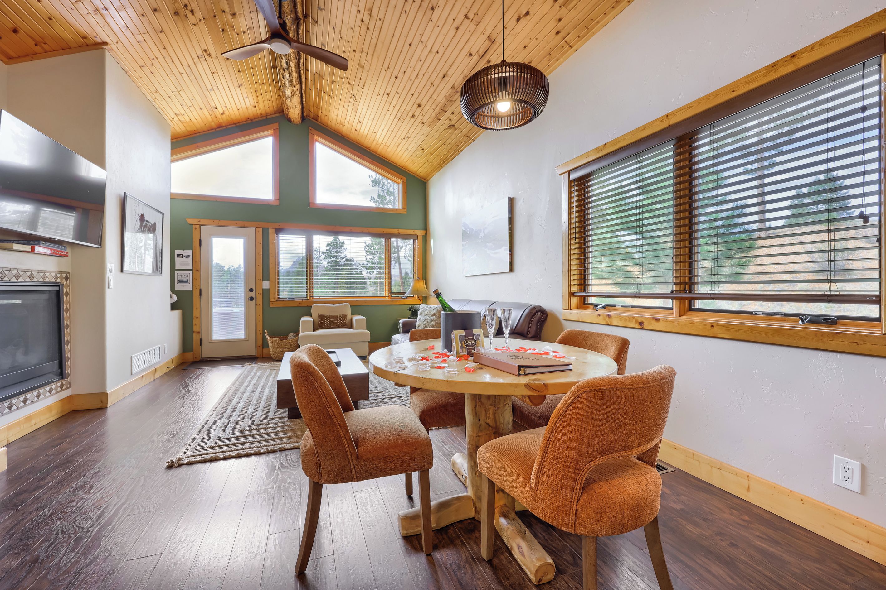 A cozy dining area with a round table, wooden chairs, and a view of the outdoors through large windows.