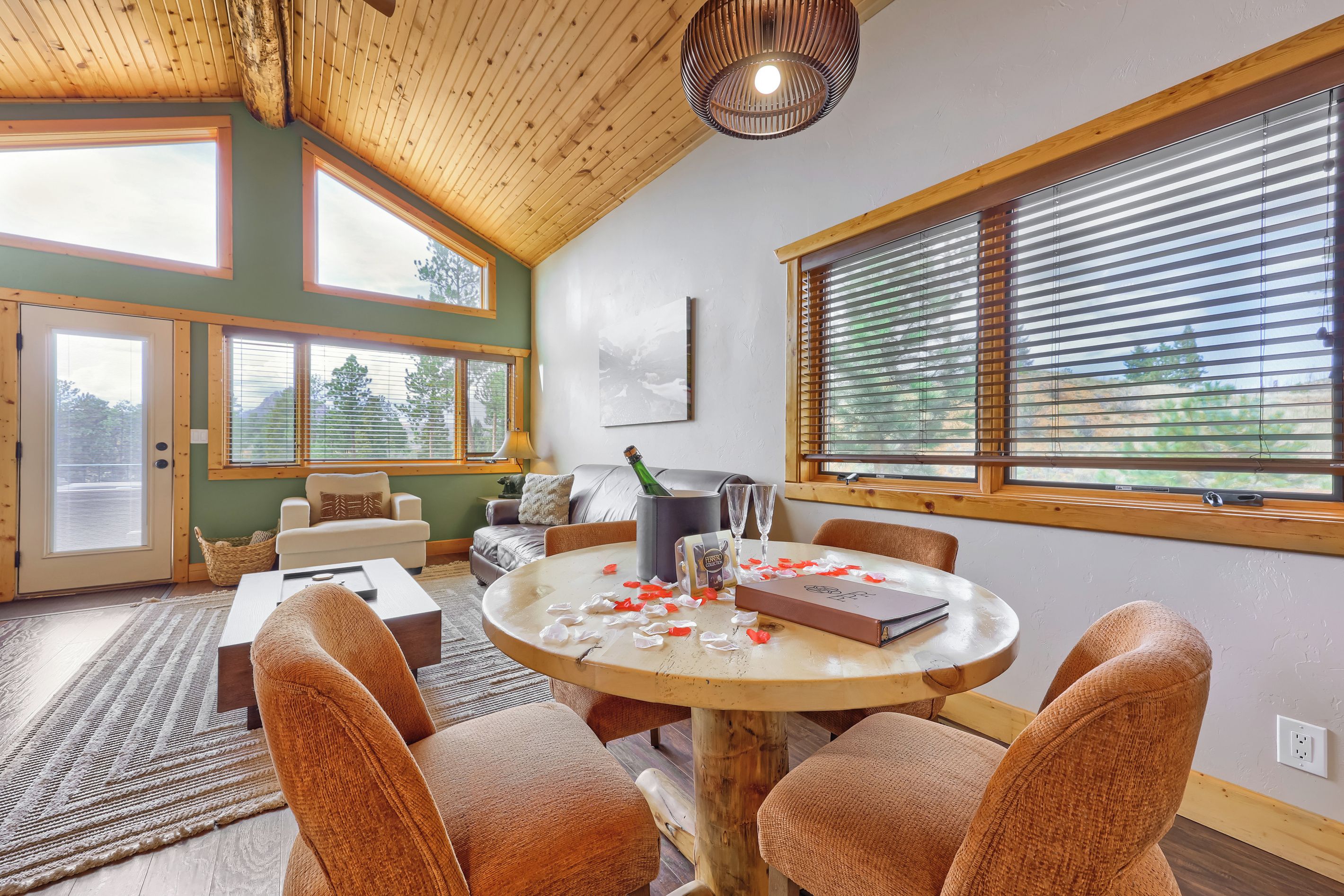 A cozy room with a wooden ceiling, large windows, a round table with chairs, and a fireplace.