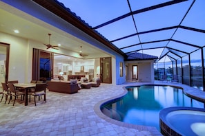 Un área junto a la piscina con una piscina curva, mobiliario exterior y un porche cubierto.
