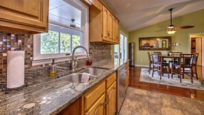 A kitchen with wooden cabinets, granite countertops, a stainless steel sink, and a dining area with a table and chairs. - Peaceful Lakefront, Spectacular View, Spacious 2 Level, 30 Min from Auburn (Alexander City)