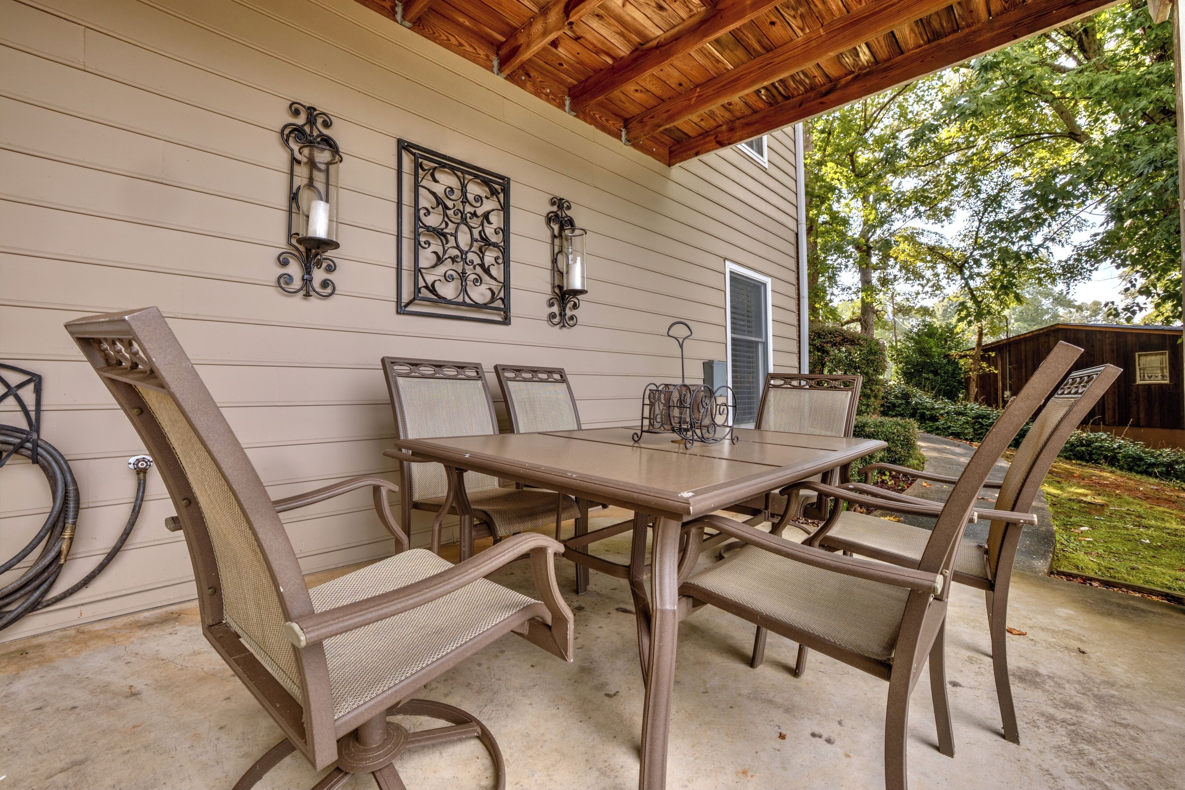 An outdoor patio with a wooden table and chairs, surrounded by a wooden pergola.
