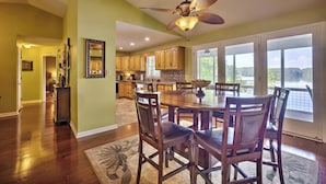 A spacious dining area with a large wooden table and chairs, a ceiling fan, and a view of a lake through large windows. - Peaceful Lakefront, Spectacular View, Spacious 2 Level, 30 Min from Auburn (Alexander City)