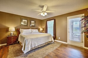 Une chambre à coucher comprenant un lit, deux tables de chevet, un ventilateur de plafond et une fenêtre avec des stores.