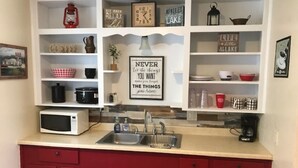 A kitchen with white shelves, red cabinets, a microwave, and various kitchen items. - Cabin at Texas Hills RV Haven on Lake Buchanan (Tow)