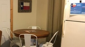 A dining area with a wooden table and white chairs, a refrigerator with a Texas flag and a menu, and a door in the background. - Cabin at Texas Hills RV Haven on Lake Buchanan (Tow)
