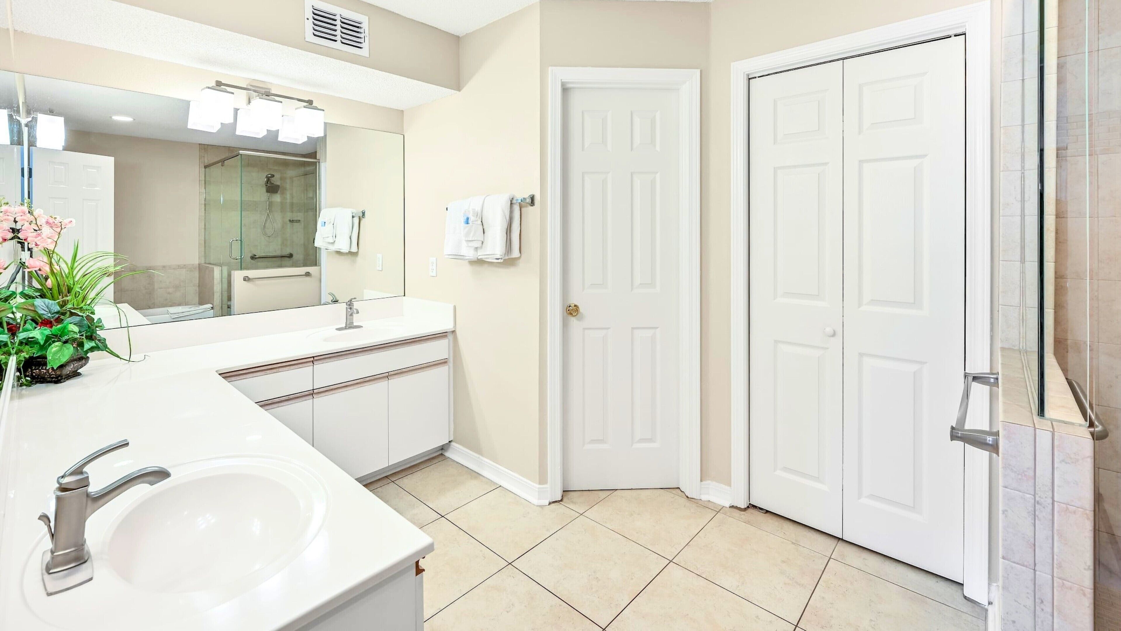 Baño con lavamanos, espejo, ducha y dos puertas.