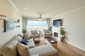 Relax in this stylish living room with a sofa set, armchairs, and a fireplace, offering a view of the beach.