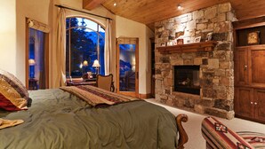Une chambre avec une cheminée en pierre, un plafond en bois et un grand lit recouvert d’une couverture verte.