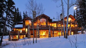 Un grand chalet à étages, doté d’une façade en pierre, de nombreux balcons et d’une lumière chaleureuse qui émane de l’intérieur.